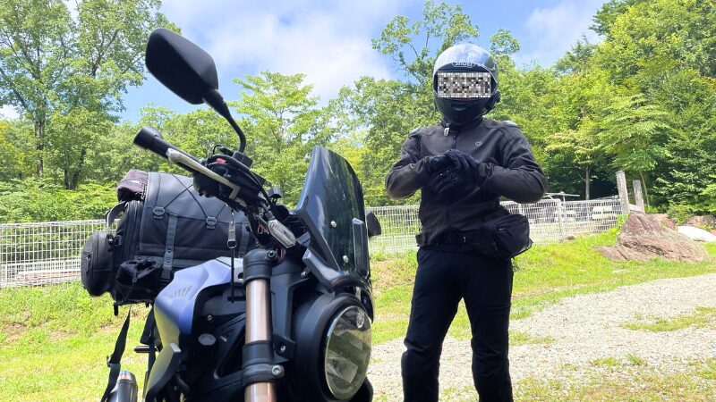 夏の林道で、プロテクター入りジャケットを着用して青いCB250Rの横に立つライダー。「夏こそプロテクター! ガチ勢ライダーの装備術」という解説テキストが赤い丸で強調されている。バイク安全装備の重要性を伝えるブログのアイキャッチ。