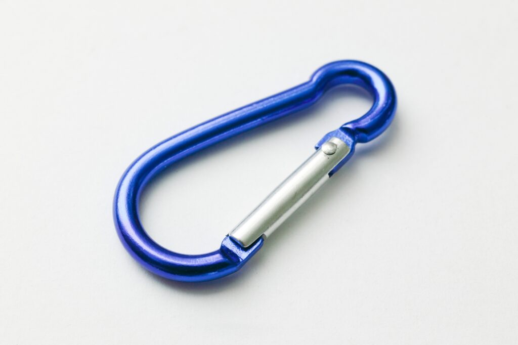 白背景の上に置かれた、青いメタリックなアルミ製カラビナ。キャンプや登山などのアウトドア用品として、またはキーホルダーなどの日用雑貨としての使用イメージを具体化する製品写真。