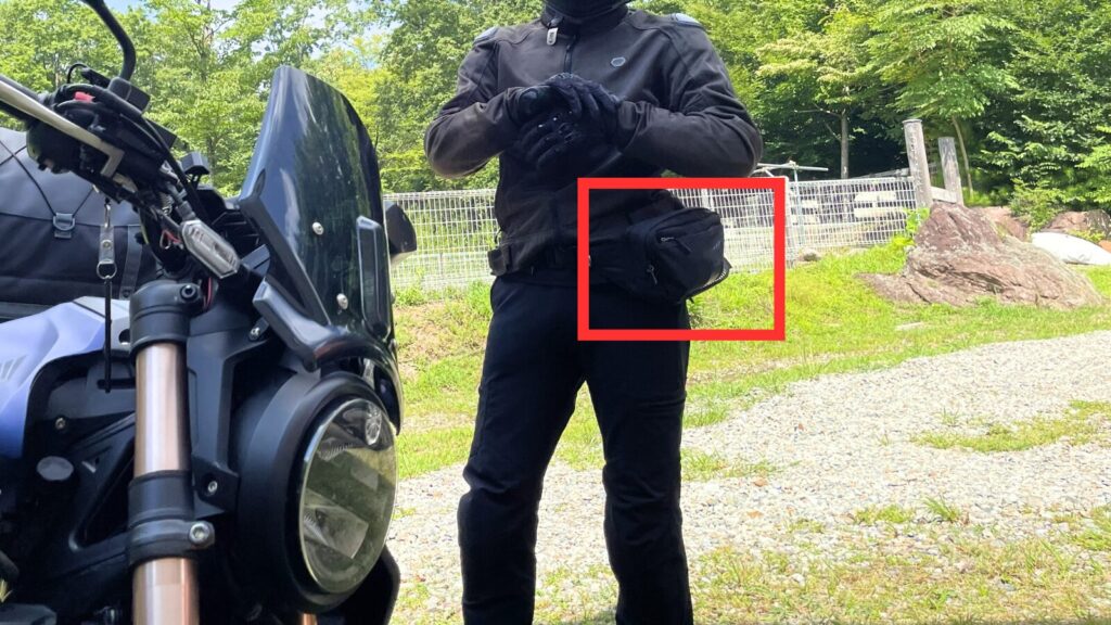 バイク用ホルスターバッグ(レッグバッグ)を腰に装着したライダーの姿。赤い枠でバッグを強調し、ライディング中の小物収納に便利な装備としての活用例を示している解説図。