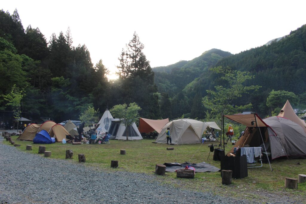WOODSMAN CAMPGROUNDの広大なメインサイト。豊かな山並みを背景に、様々なテントやタープが美しく並ぶ開放的で賑やかなオートキャンプエリア。