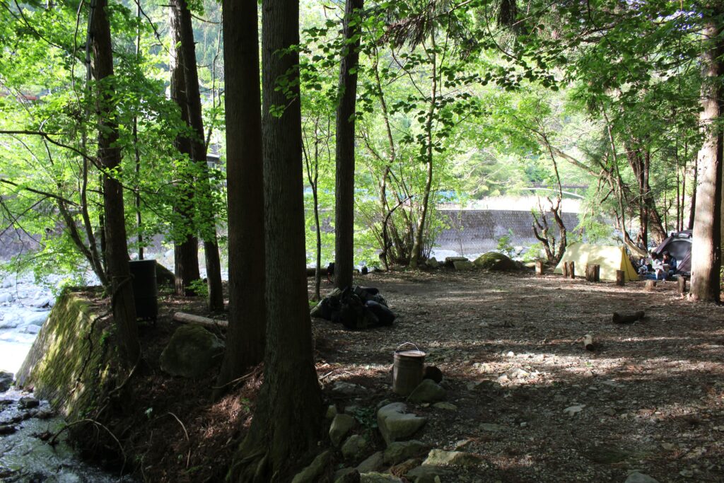 WOODSMAN CAMPGROUNDの川沿いソロサイト。木立の合間から道志川を望む木陰の平地に、ソロテントが静かに佇む自然豊かなロケーション。