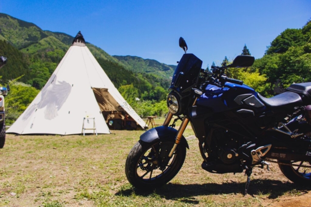 WOODSMAN CAMPGROUNDのメインサイトに設営された白いワンポールテントと、手前に力強く佇む愛車CB250R。道志の自然に映える洗練されたバイクキャンプのスタイル実例。