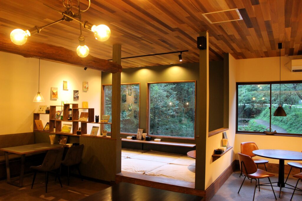 カフェ「Clover」の店内。木の天井と暖色の照明、窓の外に緑が見える